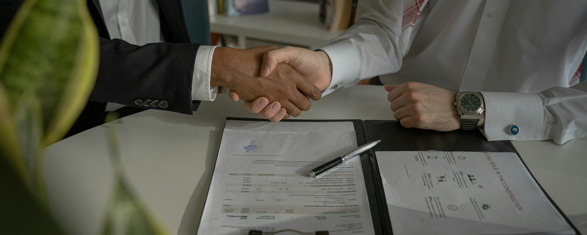 Two people shaking hands over a signed agreement